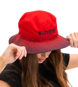 A red bucket hat with a logo, featuring a wide brim and a stylish design held by a person.