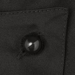 A close-up of a black button on dark fabric, part of a clothing accessory. Features visible stitching and texture.