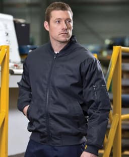 A man wears a black jacket with a zipper and side pockets, featuring one with a logo on the sleeve.
