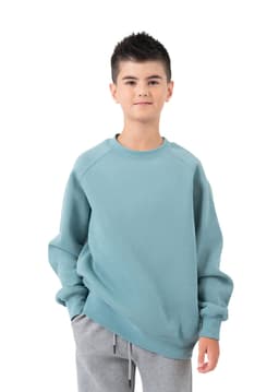 A boy wearing a light blue cotton sweatshirt, paired with grey sweatpants, standing against a white background.