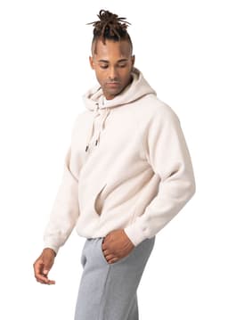 A light beige kangaroo hoodie featuring a front pocket, worn by a model with grey pants. The hoodie has a logo.