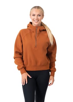 A woman wearing an orange half-zip jumper with a hood, paired with black leggings. The jumper has a logo.