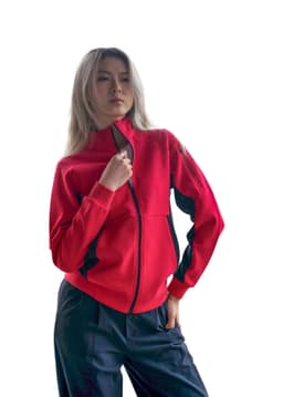 A woman wearing a red jacket with black accents, featuring a zippered front and a logo on the sleeve.