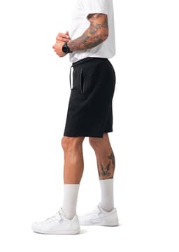 Men's black cotton sandwich shorts with an elastic waistband and pockets, modelled by a person wearing a white T-shirt and sneakers.