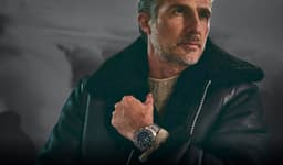 A man wearing a stylish black leather jacket and sweater, showcasing a Garmin MARQ Aviator Gen 2 watch with a silver colour.