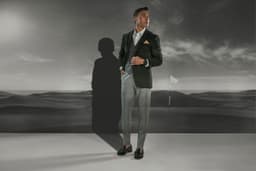 A man in a black suit stands against a landscape backdrop, wearing a Garmin Marq Golfer watch in a stylish setting.