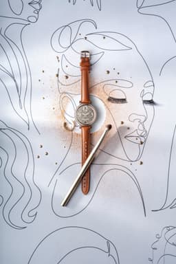 A brown leather strap watch with a silver face and a simple logo, placed on a light background with abstract line art.