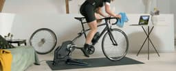 A cyclist on a black bike using a Garmin Tacx FLUX 2 Smart Trainer on a mat in a stylish room.