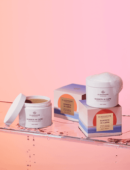 A body cream in a white jar, with a pastel box featuring soft peach and sea breeze colours, set against a gradient background.