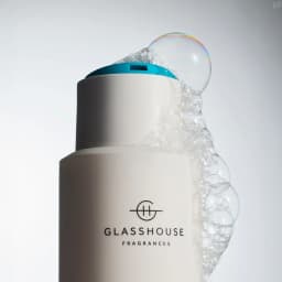 A bottle of white body wash with a turquoise lid, featuring bubbles and a logo.
