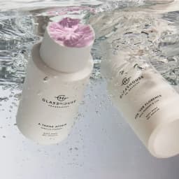 A white bottle of Glasshouse Body Wash "A Tahaa Affair" with a purple cap submerged in water, featuring a logo.