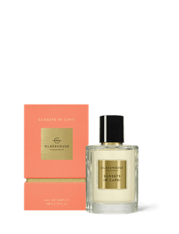 A glass perfume bottle with a black cap, containing a light yellow fragrance, next to a peach-coloured box with branding.
