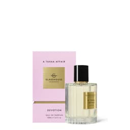 A clear glass bottle of perfume with a gold label, accompanied by a pink box featuring a gold logo.