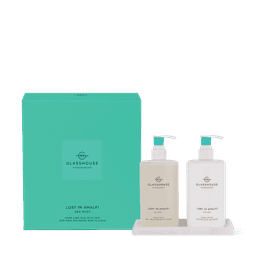 A green box containing two clear bottles of hand wash and hand lotion, with a pump dispenser, on a white tray.