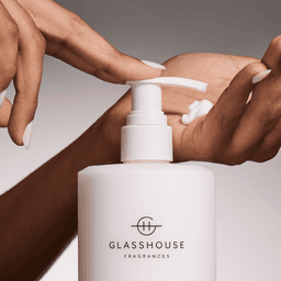 A white pump bottle of Glasshouse hand lotion with a creamy lotion being dispensed onto a hand.