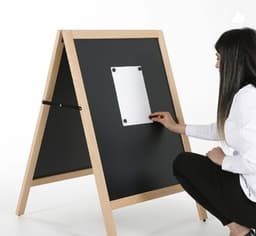 A magnetic black chalkboard A-frame with a wooden frame, being used by a person to attach a note.
