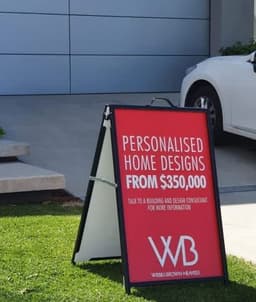 A-frame sign with a red background, promoting personalised home designs. It has a logo and is displayed on a lawn.
