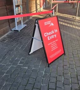 A-frame sign with a red background, featuring information for check-in entry, set on a cobblestone path.