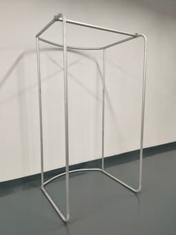 A silver tension fabric change room frame with a rectangular base and open top, set against a plain wall.