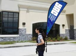 A person carrying a blue teardrop banner backpack with a logo outside a building.