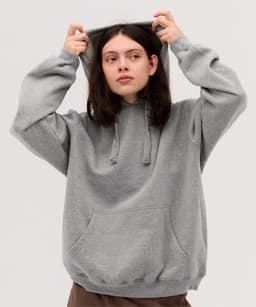 A woman in a grey hoodie pulls the hood up, featuring a front pocket and a relaxed fit.