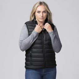 A woman wearing a black padded baffle vest over a grey long-sleeve top, with her hands at the collar.