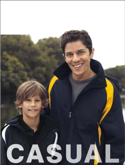 A reversible sports jacket in navy and yellow, worn by a man and a boy outdoors near water, with a logo on the jacket.