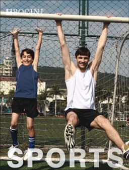 A man and a boy hanging from a goal post, both wearing singlets; the man in white and the boy in blue.