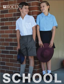 A boy in a white school shirt and grey shorts stands next to a girl in a blue shirt and black skirt, both smiling.