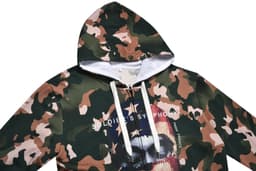 A 100% cotton hoodie in a camouflage pattern, featuring a large graphic print and a logo on the front.