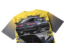 A racing tee featuring a graphic design of a dark car against a yellow and grey background. It includes a logo.