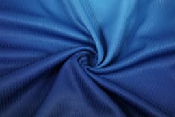 A jersey fabric in shades of blue, showcasing a textured, swirling pattern, suitable for a soccer uniform.