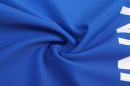 A close-up of a blue fabric, featuring a smooth texture and a prominent white branding logo.