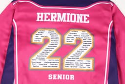 A pink varsity jacket featuring gold lettering and a list of names on the back, including "Hermione" and "22."
