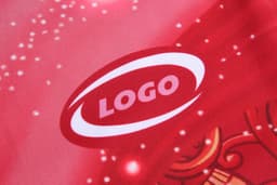 A close-up of a red fabric featuring a logo with a subtle design, suitable for a sports uniform.