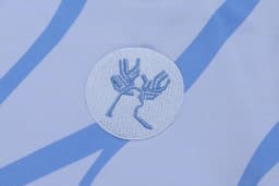 A hoodie featuring a circular embroidered logo in light blue and white, set against a patterned background.