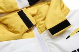 A close-up of a puffer coat featuring yellow and white fabric, with removable sleeves and a hood, and a logo in the design.