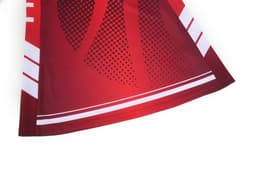 A netball dress in vibrant red with a pattern of dots and stripes, featuring a logo on the fabric.