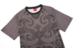 A grey jersey with intricate black patterns and a logo at the collar. It has short sleeves and a round neck.