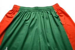 Green and orange junior soccer shorts with an elastic waistband and a logo on one side.
