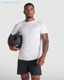 A man wearing a white Montecarlo T-shirt and black shorts holds a fitness ball, posing against a light background.