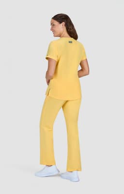 A woman wearing a yellow top and matching pants, standing with her back to the camera. The outfit has a logo on the back.
