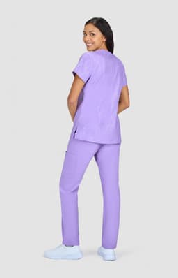 A woman wearing a purple printed top and matching purple pants, standing against a grey background.