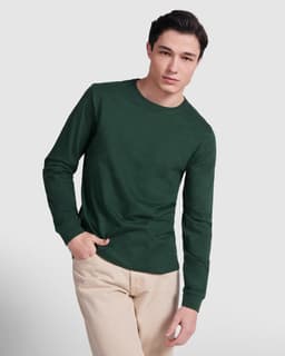 A green long-sleeved T-shirt displayed on a model, paired with light-coloured pants. The shirt features a logo.