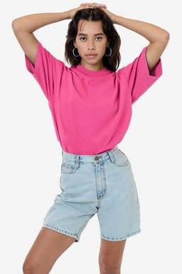 A pink short sleeve crewneck t-shirt paired with light denim shorts. The model poses with arms raised.