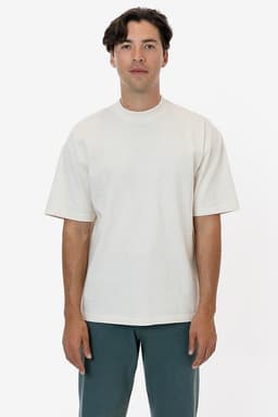 A man wearing a short sleeve, garment-dyed crewneck tee in a light beige colour, standing against a white background.