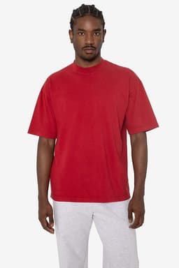A short sleeve crewneck tee in red, featuring a relaxed fit and a logo. Model is wearing grey pants.
