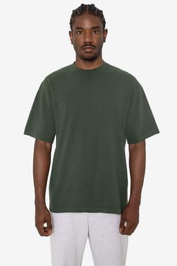 A green short sleeve crewneck tee with a loose fit, featuring a logo. Model wearing grey sweatpants.