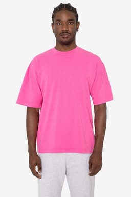 A pink short sleeve crewneck tee worn by a model, paired with grey sweatpants. The tee features a logo.