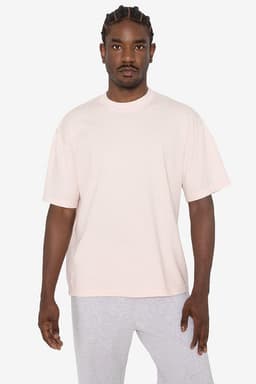 A short sleeve crewneck t-shirt in a soft pink colour, worn by a model with braided hair. Features a logo.